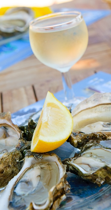 Dégustation d'huîtres et vin blanc frais Huîtres fraîches sur un plateau avec un quartier de citron, accompagnées d'un verre de vin blanc frais en arrière-plan.